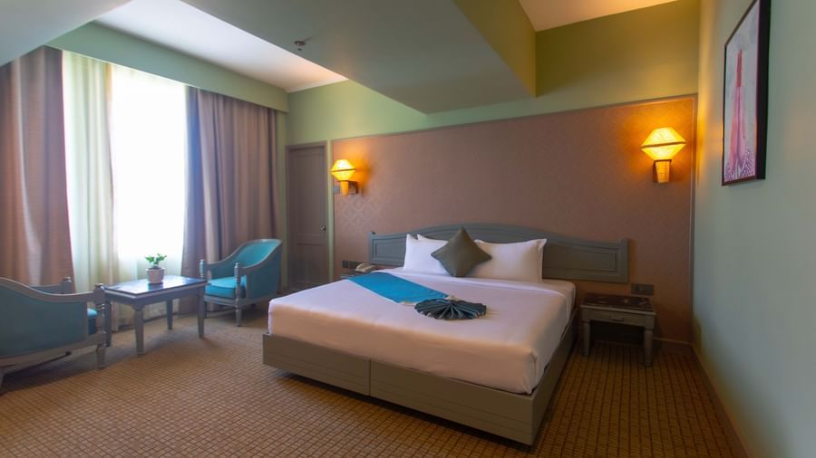 A hotel room at Shilton International, Kochi, with a large bed, a comfortable seating area, and large windows.
