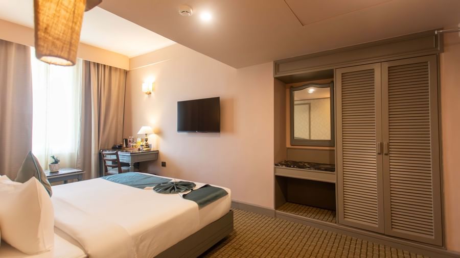  A guest room at Shilton International, Kochi, with a bed, wall-mounted television, and a built-in wardrobe.