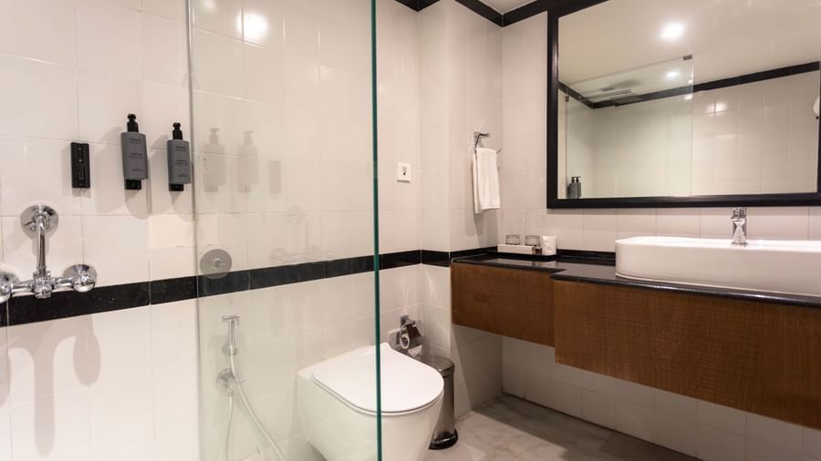 A contemporary bathroom at Shilton International, Kochi, with a glass shower, wall-mounted toilet, and large vanity.