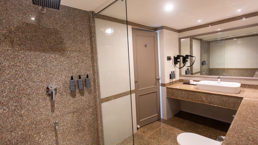 A bathroom at Shilton International, Kochi, featuring a rainfall shower, large vanity, and modern fixtures.