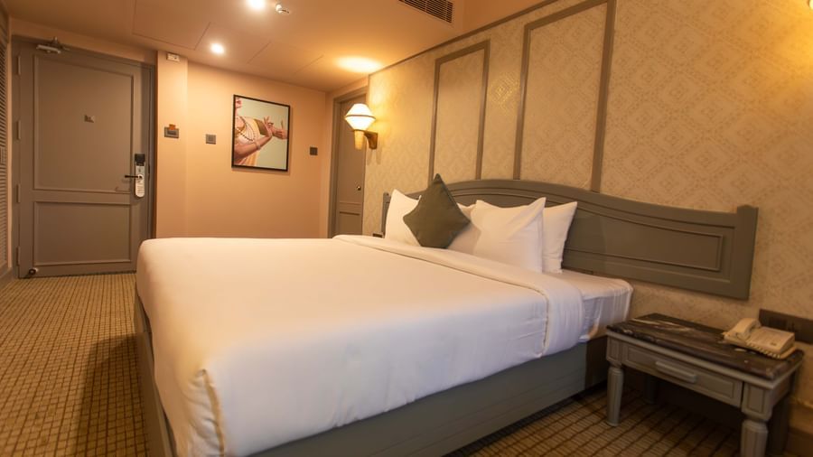  A guest room at Shilton International, Kochi, with a large bed, bedside table, and a closed door.