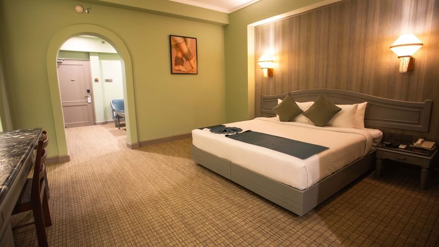  A guest room at Shilton International, Kochi, with a bed, a desk, and an arched doorway leading to another area.