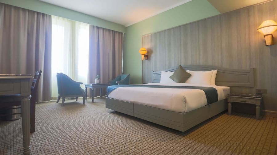  A guest room at Shilton International, Kochi, with a large bed, seating area, and a desk by the window.