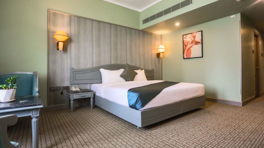 A guest room at Shilton International, Kochi, with a large bed, a desk area, and wall decor.