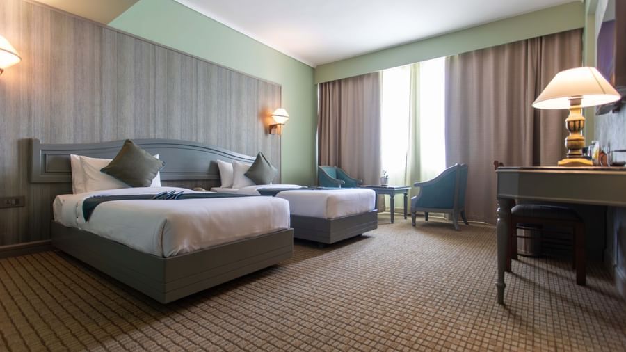  A guest room at Shilton International, Kochi, with two beds, a desk, and a seating area by the window.