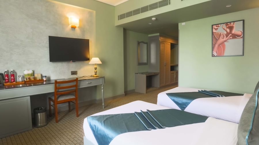  A guest room at Shilton International, Kochi, with two beds, a desk, and a wall-mounted television.