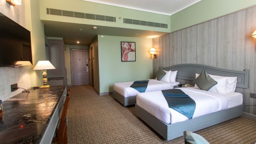  A guest room at Shilton International, Kochi, with two beds, a desk, and a wall-mounted television.
