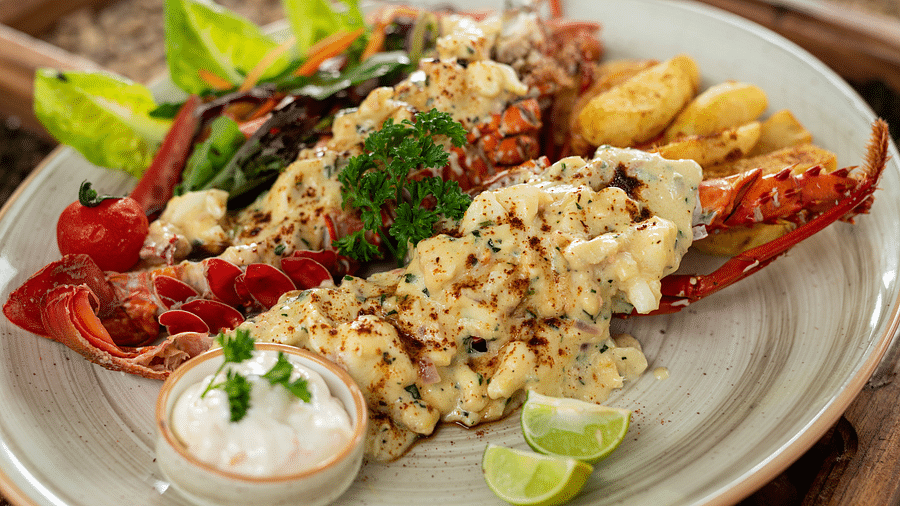 A close-up of a lobster dish topped with a creamy seafood mixture, served with roasted potatoes and a side of dipping sauce at Shooting Star Boutique Hotel