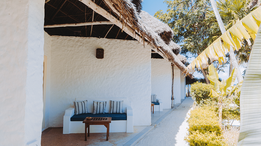 Exterior view of a building with a thatched roof overhang, featuring a small patio with a cushioned bench and a wooden table - Shooting Star Boutique Hotel.