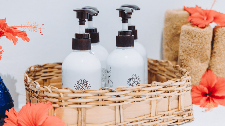 Close-up of a basket holding four pump bottles of lotion and wash clothes, with hibiscus flowers surrounding the basket.