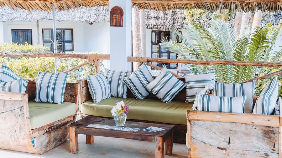 Outdoor lounge area under a thatched roof with wooden furniture and striped cushions, surrounded by tropical plants - Shooting Star Boutique Hotel.