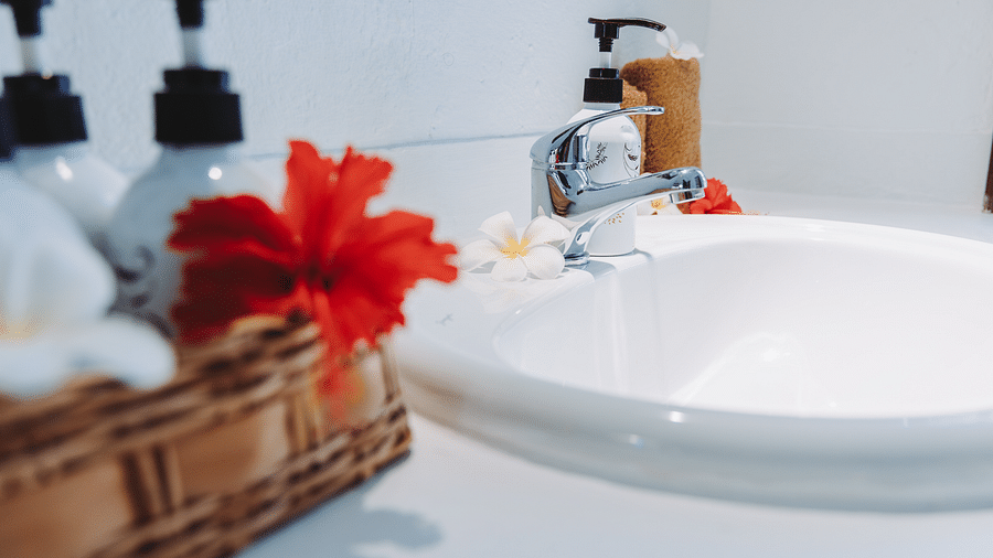 Close-up of a bathroom sink with a hibiscus flower, white flowers, and soap dispensers - Shooting Star Boutique Hotel.