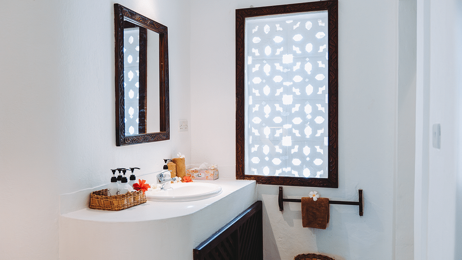 A bathroom interior featuring a white countertop with a sink, a rectangular mirror, and a window with a patterned screen - Shooting Star Boutique Hotel.