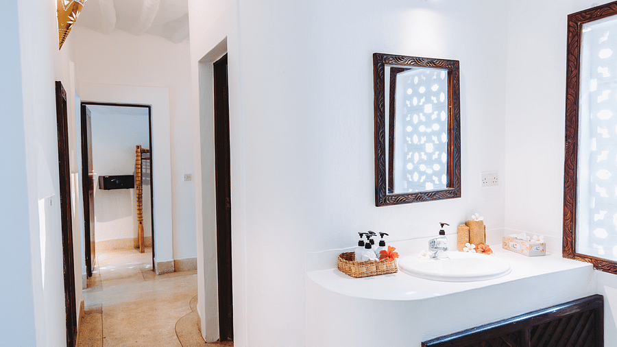 Interior view of a modern white bathroom featuring a sink with toiletries, two dark wood framed mirrors, and a hallway in Sea View Family Cottages - Shooting Star Boutique Hotel.