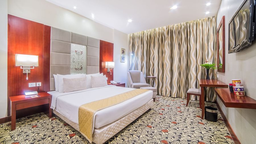 A spacious hotel room with crisp white bedding, a work desk, and tasteful deco A grand hotel suite with an opulent red and white decor, large bed, and seating area, reflecting a traditional style at Sitara Luxury Hotel in Hyderabad near Ramoji Film City.