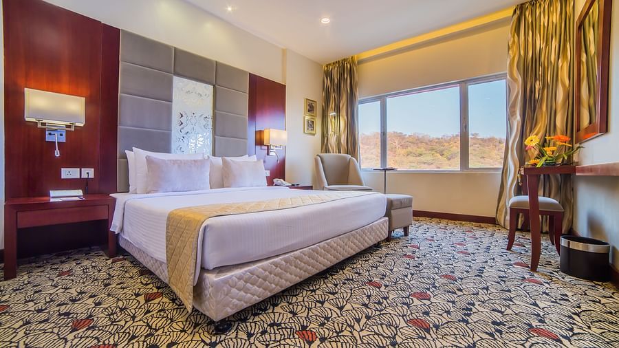 A luxurious hotel room with a plush white bed, warm accent lighting, and a scenic window view A grand hotel suite with an opulent red and white decor, large bed, and seating area, reflecting a traditional style at Sitara Luxury Hotel in Hyderabad near Ramo
