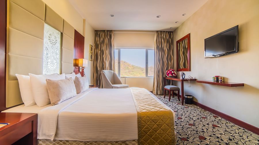 A bright and airy hotel bedroom with plush bedding and a view of the desert landscape at  Sitara Luxury Hotel in Hyderabad near Ramoji Film City.