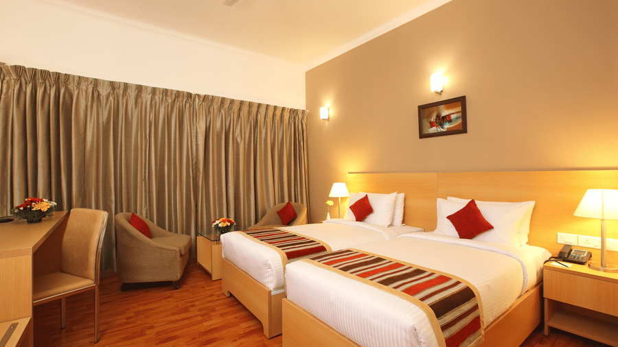 A Premium Room at Starlit Suites, Kochi, featuring twin beds, a desk, an armchair, and warm lighting.