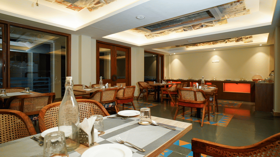 A dining table set with plates and cutlery in a restaurant setting with warm lighting | Sukama Resort & Spa, Mukteshwar