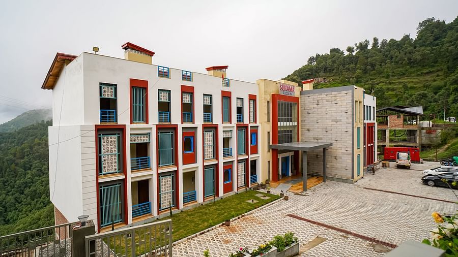 An aerial view shows a multi-story building complex with red and white facades situated on a hillside | Sukama Resort & Spa, Nainital