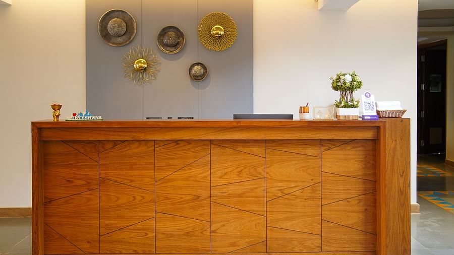 A close-up view of a wooden hotel reception desk with decorative wall art above it | Sukama Resort & Spa, Nainital