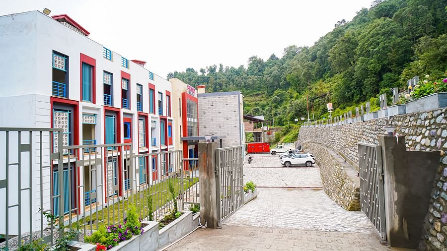 A pathway leads towards a contemporary building complex with colourful elements, set against a backdrop of green mountains | Sukama Resort & Spa, Nainital