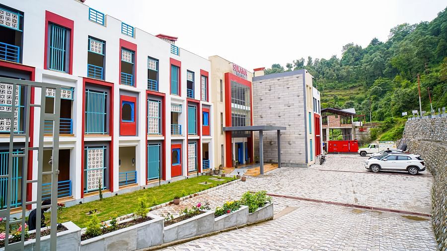 The exterior of a modern building with red and white sections and a paved courtyard is visible | Sukama Resort & Spa, Nainital