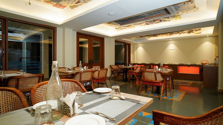 A dining table set with plates and cutlery in a restaurant setting with warm lighting | Sukama Resort & Spa, Nainital