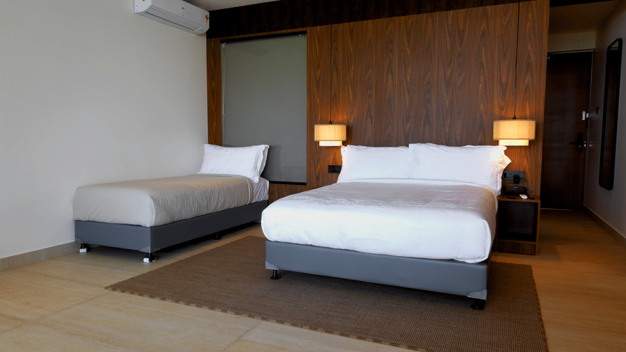A bedroom at hotel SUKAVI featuring a king size bed, a separate single bed, and a wooden headboard wall.