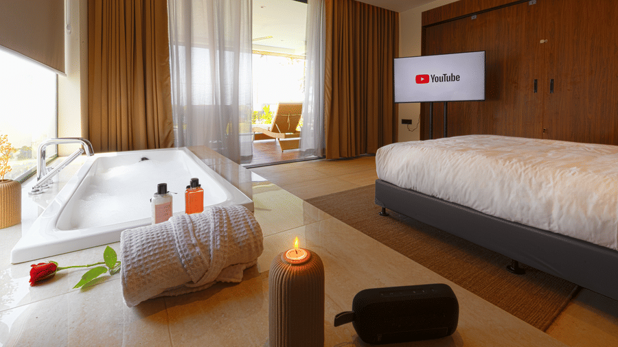 A bedroom at hotel SUKAVI with a king size bed, a television, and an open bathtub area near a window balcony.