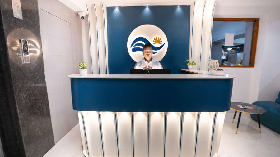View of the reception desk with a staff member standing behind it and bright lighting at Sunrise Business Hotel, Hyderabad.