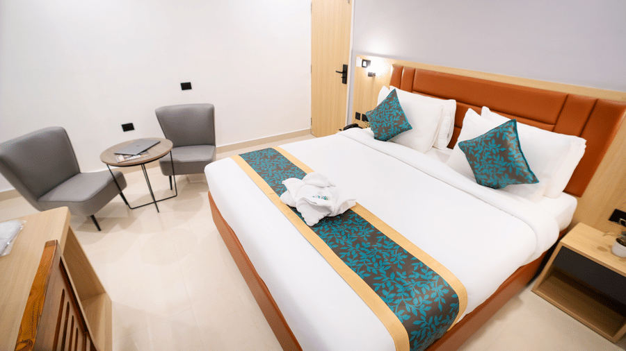 View of a spacious room with a large bed with a headboard, bedside tables on both sides, and a seating area to the side at Sunrise Business Hotel, Hyderabad.