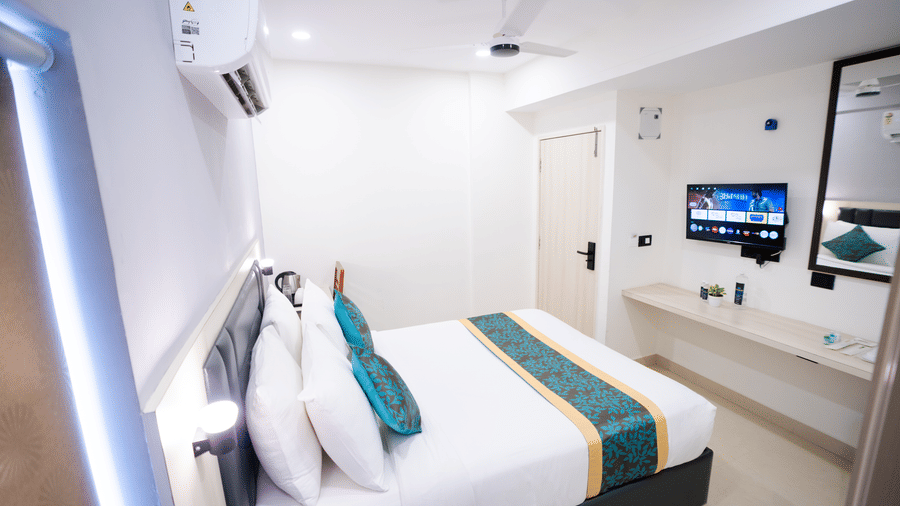 View of a large bed, wall-mounted TV, and mirror at Sunrise Business Hotel, Hyderabad.