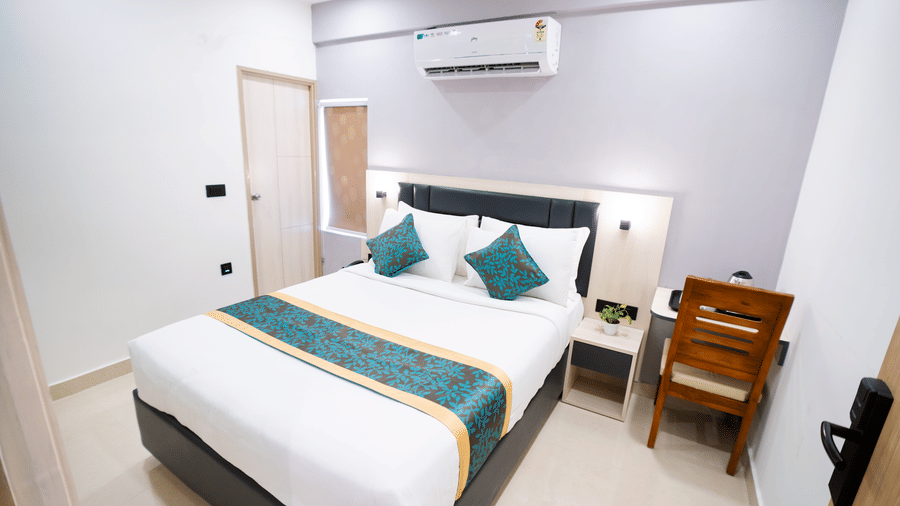A room featuring a spacious bed, wall-mounted A/C above the headboard, a mirror, and a closed door to the side at Sunrise Business Hotel, Hyderabad.