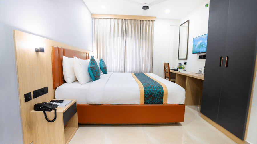 A room with a bed, cabinets, a wall-mounted television, and a side table at Sunrise Business Hotel, Hyderabad.
