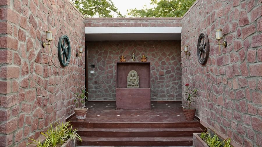 A brick wall structure with steps in the middle leading to a sculpture of a buddha in a mediation pose , lights and other decorative elements on the wall.