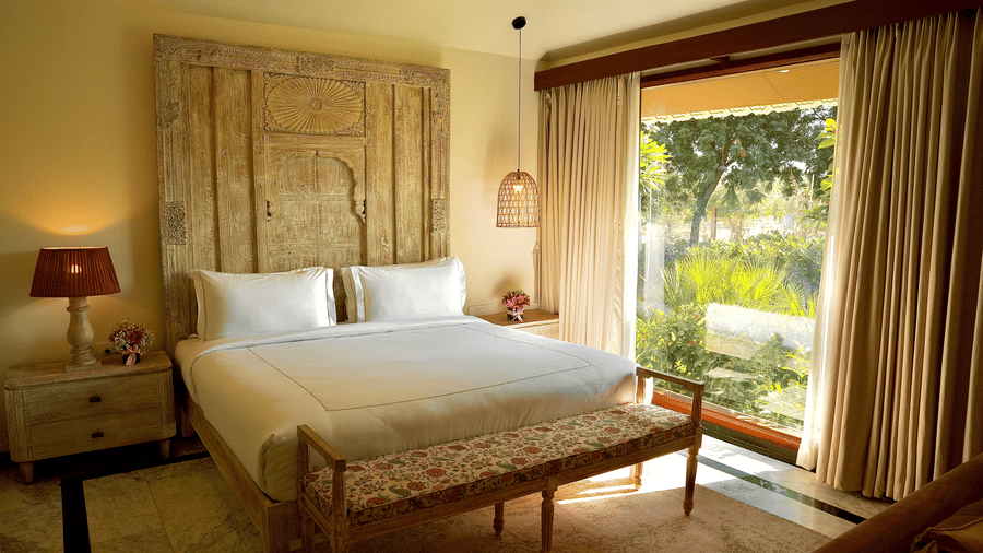 A well lit bedroom with a comfortable king size bed, wall decor and curtained windows overlooking greenery at Surpura Bagh, Jodhpur.