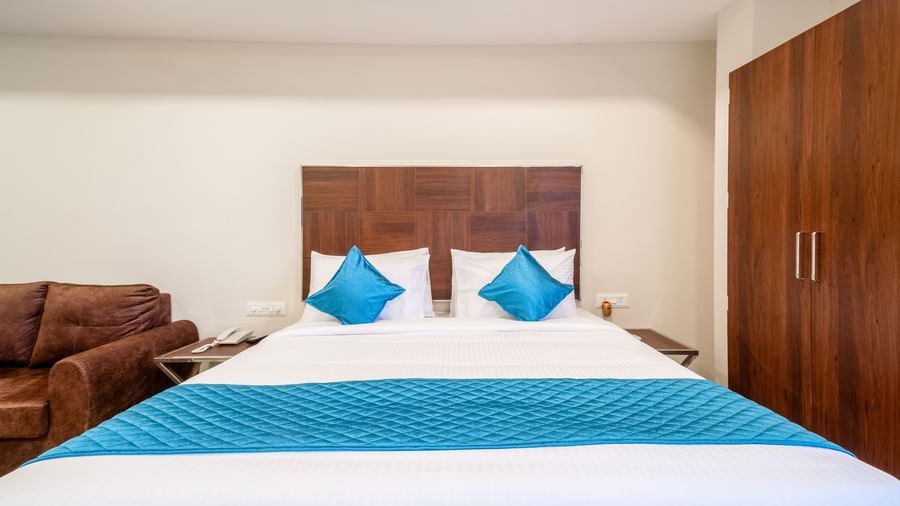 Comfortable double bed with blue cushions placed near sofa seating in a cosy modern bedroom at Swarna's The Capital.