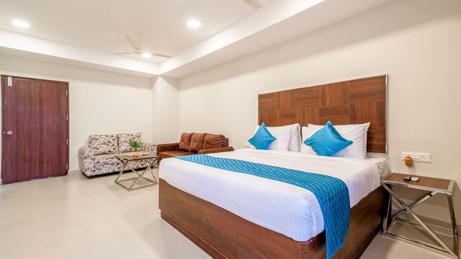 Spacious bedroom featuring double bed with blue accents seating area soft lighting and wardrobe at Swarna's The Capital.