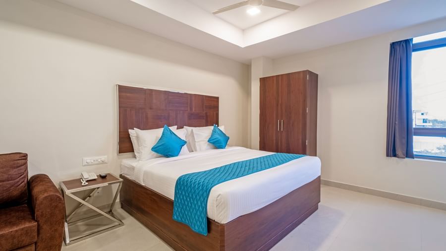 Neatly furnished bedroom with double bed side tables wardrobe and bright window in a cosy setting at Swarna's The Capital.