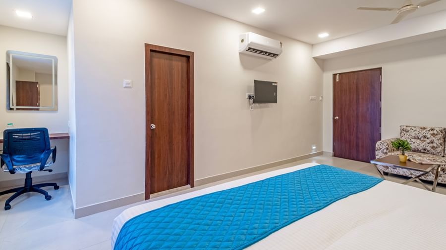 Room view with double bed blue runner wardrobe work desk television and air-conditioning at Swarna's The Capital.