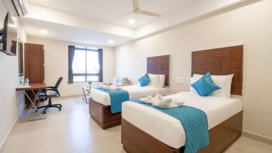 Twin beds with fresh linens blue runners seating area and bright ambience creating comfort at Swarna's The Capital.