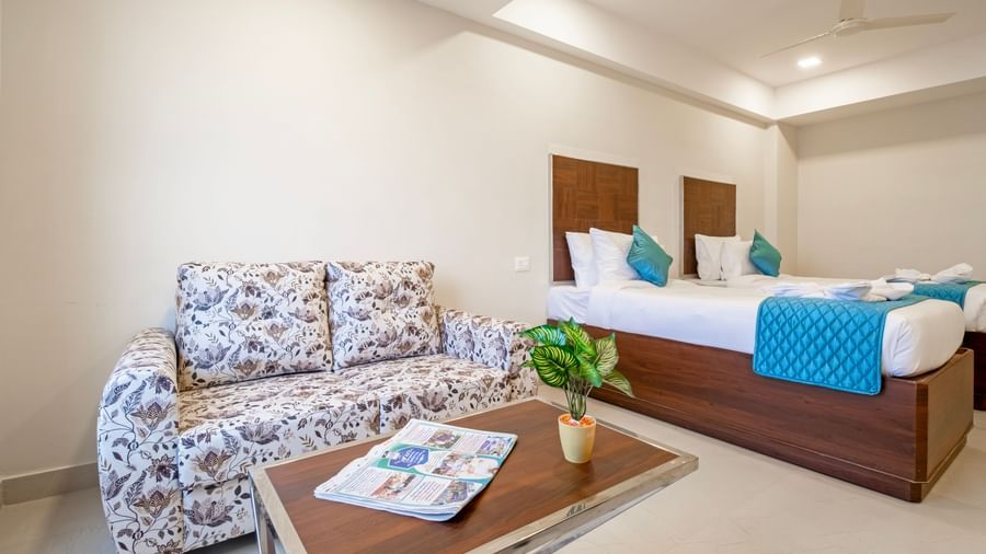 Cosy bedroom with twin beds, blue cushions, patterned sofa, glass table and indoor plants at Swarna's The Capital.