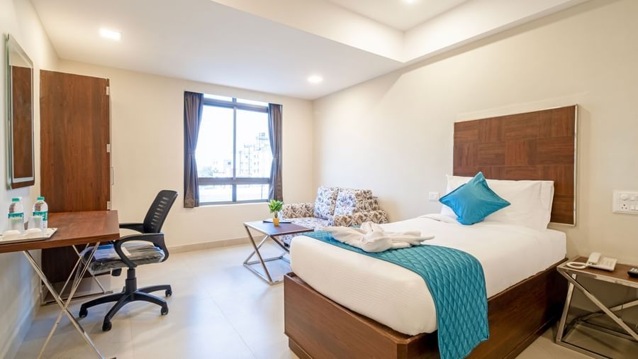 Modern room with king size beds work desk chair mirror and large window offering natural light at Swarna's The Capital.