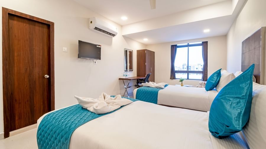 Spacious twin bed room with blue runners television wardrobe and large windows for comfort at Swarna's The Capital.