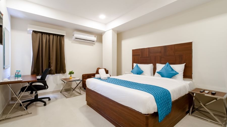 Well lit bedroom with desk comfortable chair double bed blue cushions and air-conditioning ideal for work and rest at Swarna's The Capital.