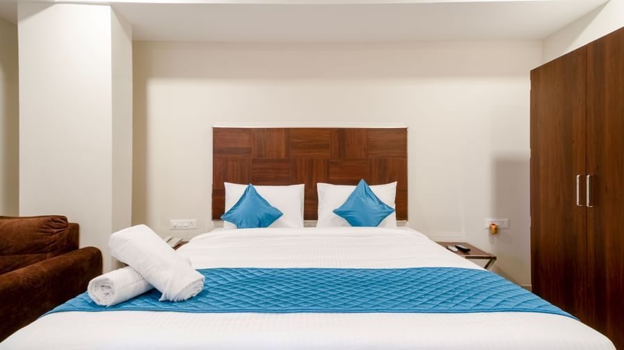 Elegant bedroom with wide bed blue accents soft pillows and wooden wardrobe offering comfort and relaxation at Swarna's The Capital.