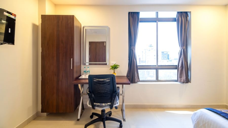 Work desk with ergonomic chair wardrobe mirror and window providing a functional and airy workspace at Swarna's The Capital.