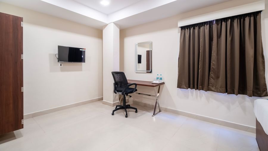 Neatly designed room with work desk chair mirror television and wardrobe in a bright setting at Swarna's The Capital.