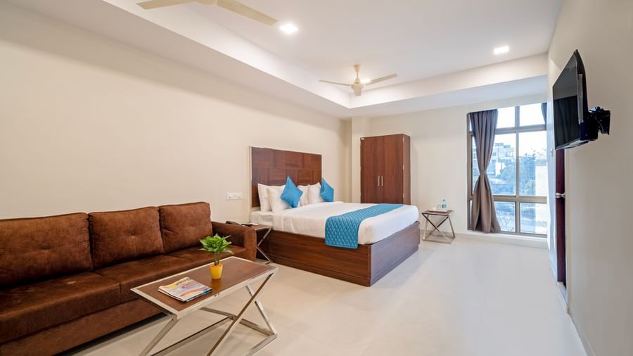 Bedroom with double bed blue decor sofa seating area television and soft lighting for a homely stay at Swarna's The Capital.